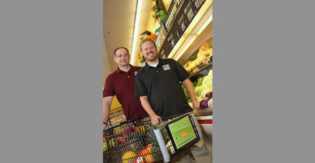 NMSU researchers Mihai Niculescu, left, and Collin Payne with a grocery cart placard used in grocery stores to study how in-store marketing can be used to influence shoppers to buy more fresh fruit and vegetables. (NMSU photo by Robert Yee)