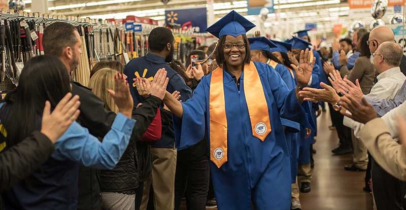 A Walmart associate receives high-fives as she enters an academy graduation.