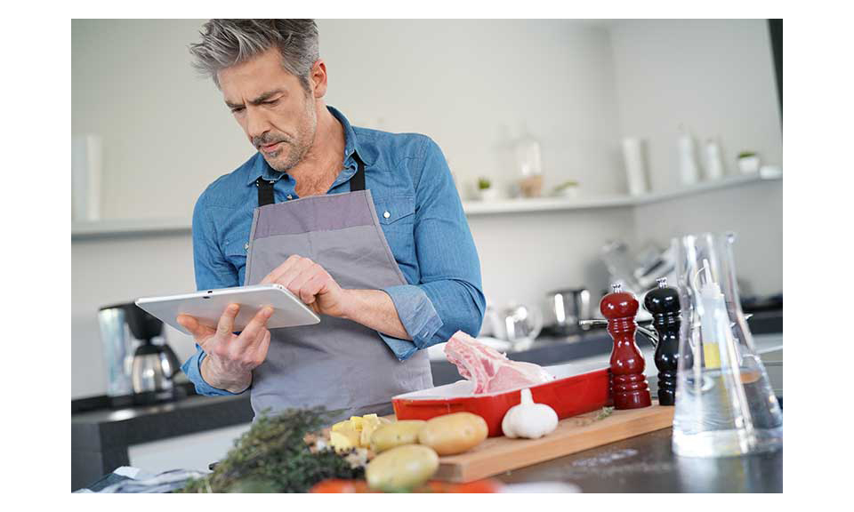 A man prepares meat using an online recipe.