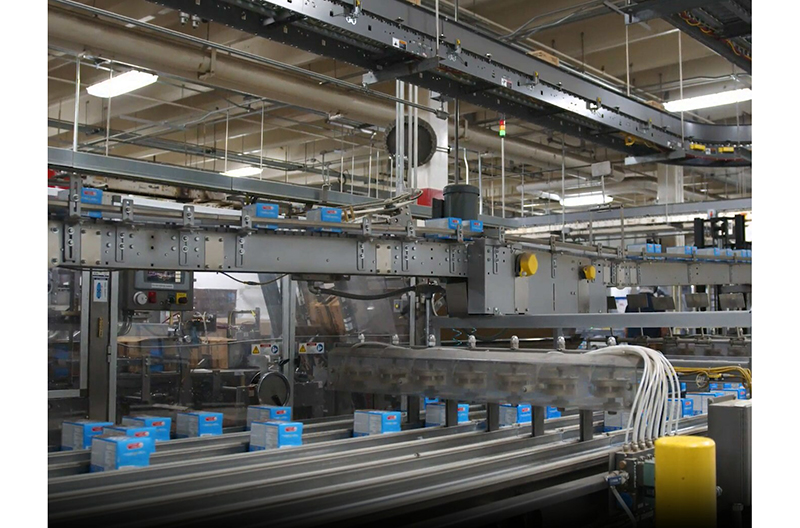 Image of the interior of a Kellanova manufacturing facility, with several blue boxes of product running down automated grey production lines.