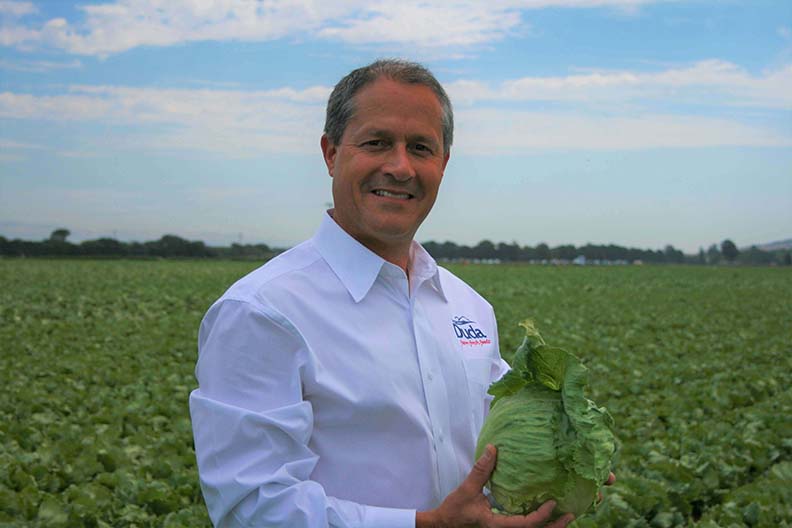 Image of Rick Alcocer holding head of lettuce in a field