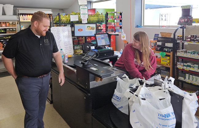 photo of Mackinaw Family Market cashier Tayler Walker assists Conner MacDonald.