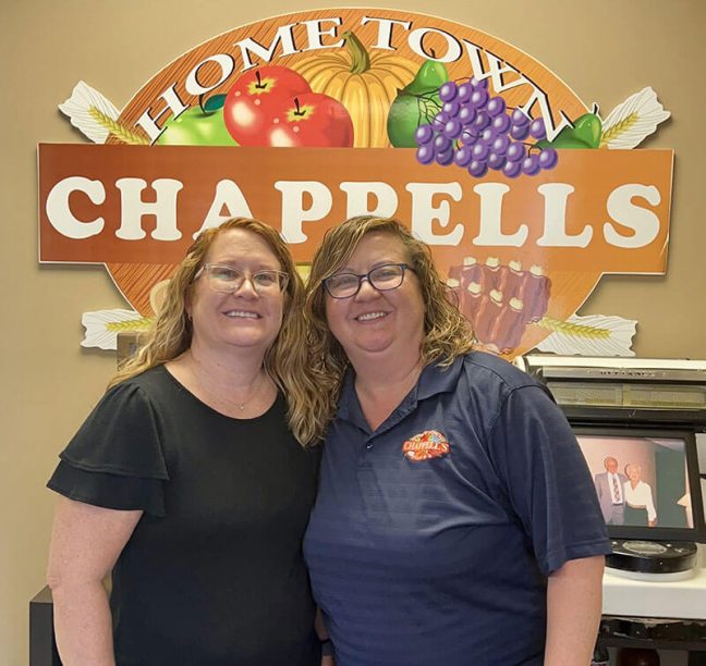 photo of Chappell’s Home Town Foods co-owners Caroline Pace and Emily Blankenship standing in front of Chappell's logo