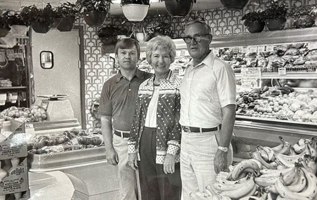 black-and-white photo of Phil Chappell with parents Kate and Jack Chappell standing in produce department