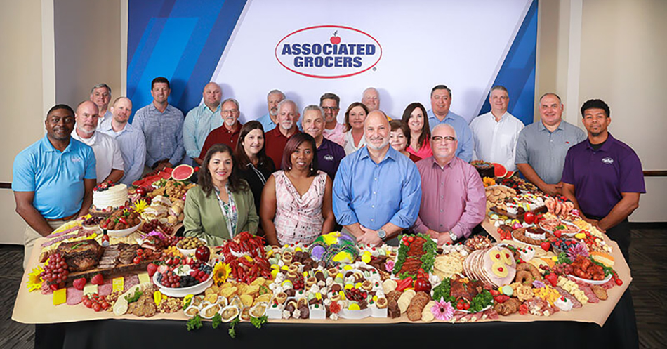 group photo of Associated Grocers team surrounded by a table filled with food