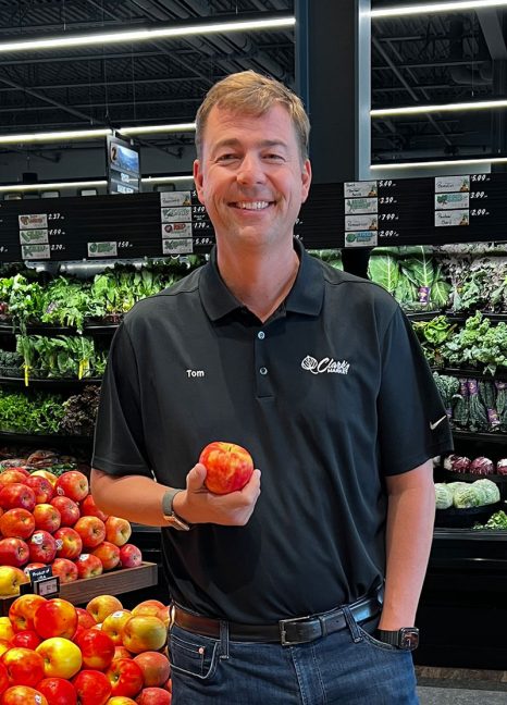 photo of Tom Clark, president of Clark’s Market, holding an apple in produce department