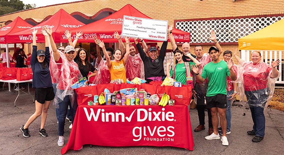photo of Winn-Dixie associates standing in front of a Winn-Dixie Gives banner and holding up a check to Feeding America for hunger relief