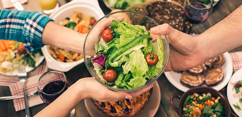 photo of table filled with food and hands passing a bowl of salad