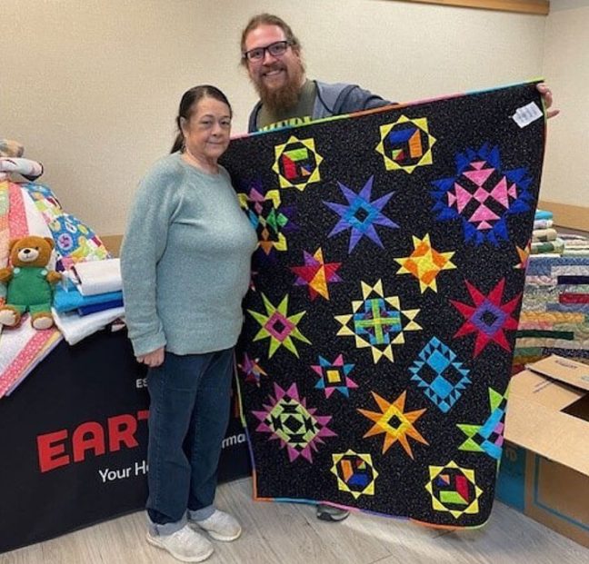 photo of woman and man displaying quilt made to help Hurricane Helene victims
