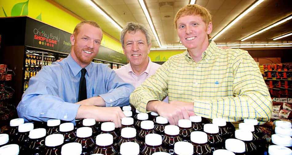 Photo of Ray Charley (center), third-generation grocer, is flanked by the fourth generation, sons Tom and Mike of Charley Family Shop ’n Save.