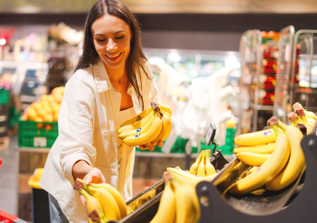 Shopper selecting a bunch of ripe bananas from a retail produce display