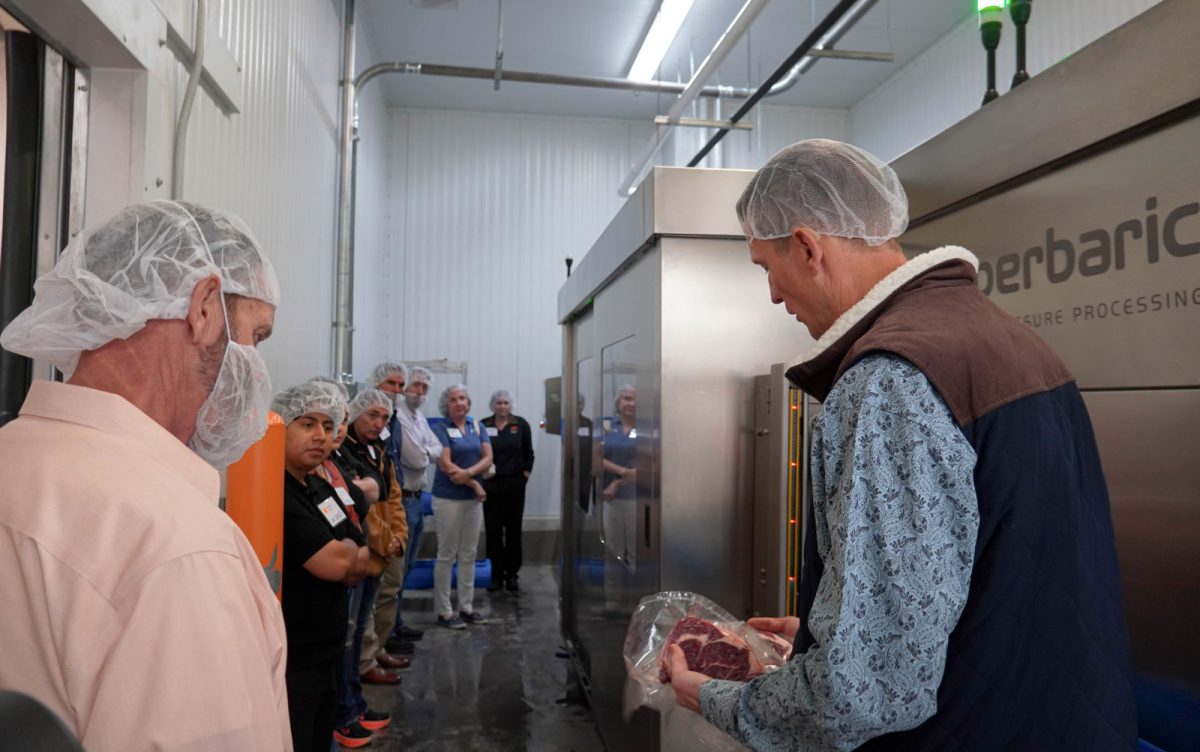 Shade Hughes demonstrates FAPC’s Hiperbaric 55 high-pressure processing machine to workshop attendees gathered around it.