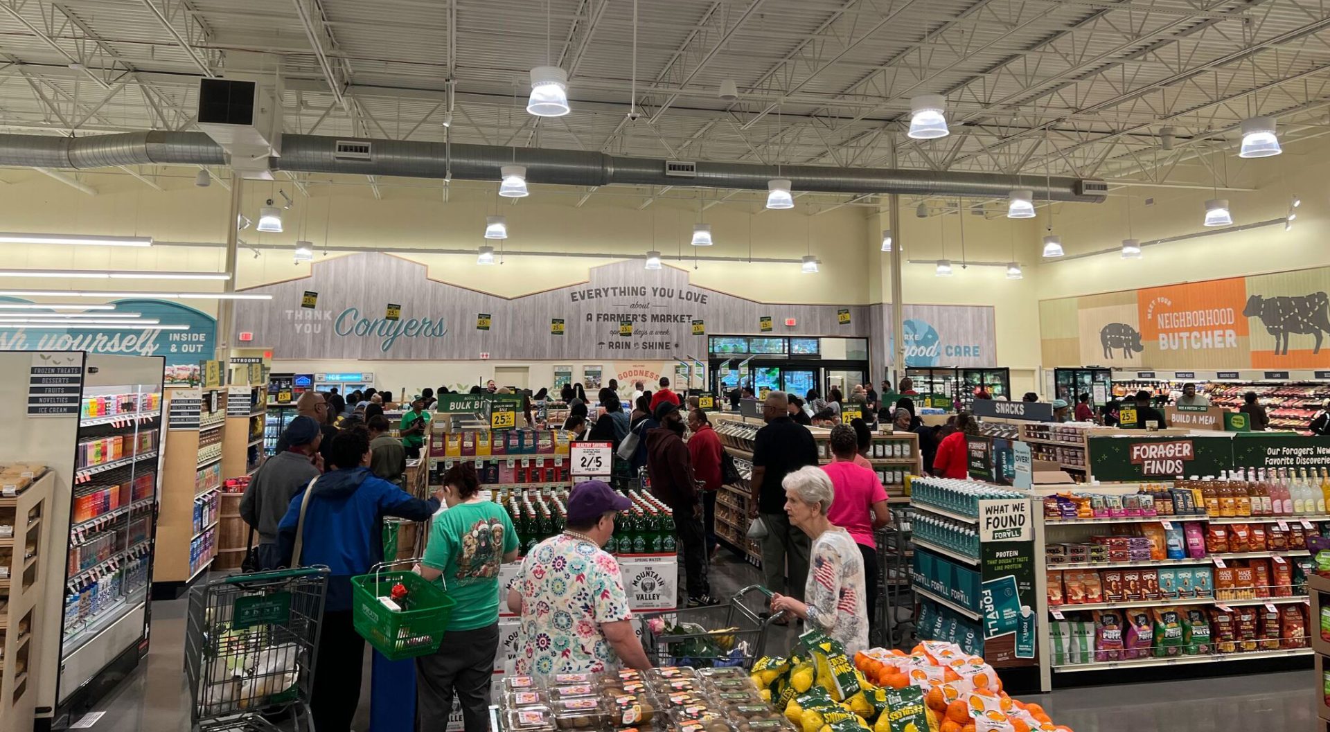 Wide view of a busy Sprouts Farmers Market interior with shoppers around produce displays under high ceilings